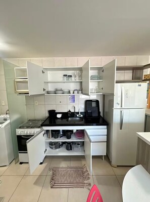 Eine kleine Küche mit weißen Schränken, einer schwarzen Arbeitsplatte, einem Herd, einer Spüle und einem Kühlschrank.