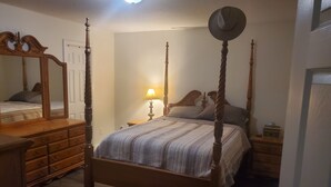 Una cama con dosel, un espejo, una cómoda, una lámpara de noche y un sombrero sobre el cabecero.
