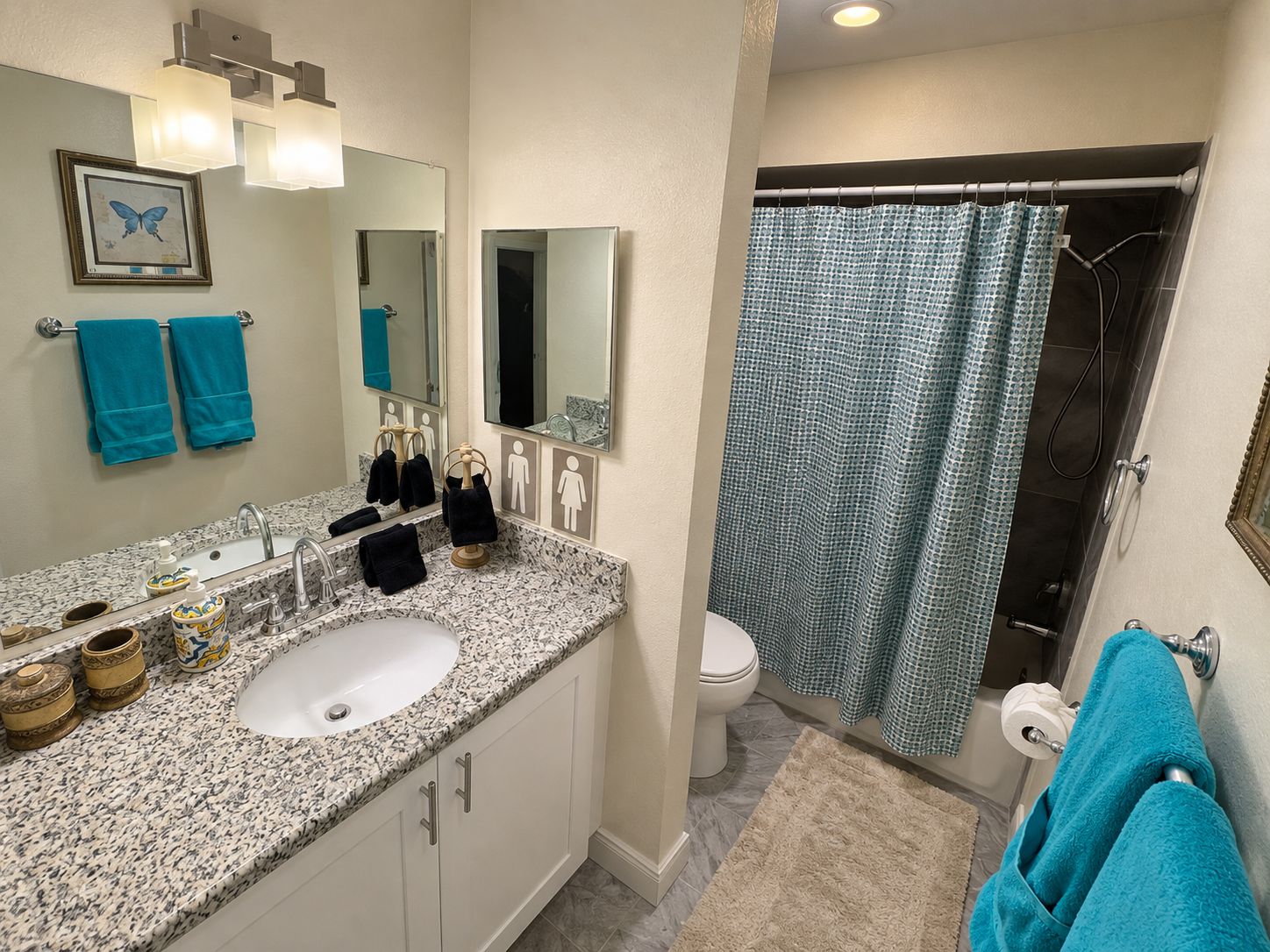 A bathroom with a granite countertop sink, two mirrors, a shower curtain, and a toilet.