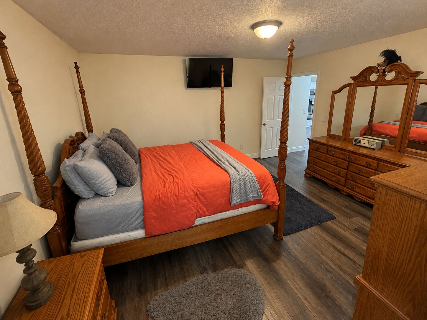 Une chambre à coucher avec un lit à baldaquin, une commode, un miroir et un téléviseur fixé au mur.