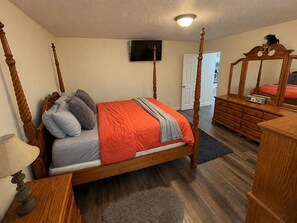 Un dormitorio con cama con dosel, cómoda, espejo y televisor en la pared.