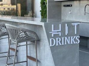 A bar area with a sign reading 'HIT DRINKS' and a modern chair. - HIT 202 - Sophisticated apartment with ocean views on Cabo Branco beach. (João Pessoa)