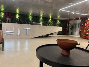 A reception desk with a 'WELCOME HIT' sign, a modern interior with a green wall, and a round table with a bowl. - HIT 202 - Sophisticated apartment with ocean views on Cabo Branco beach. (João Pessoa)