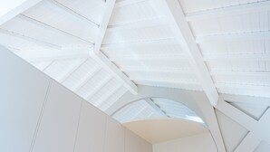 Un interno moderno con un design geometrico del soffitto e un'ampia finestra ad arco centrale.