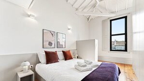 Una camera da letto moderna con un letto, cuscini, un comodino, una lampada, opere d'arte e una finestra vista.