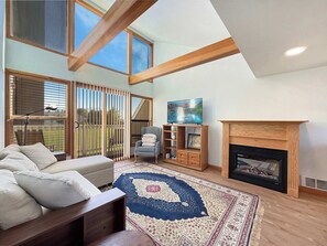A living room with a sofa, a fireplace, a television, and a large window. - Golf Course Downstairs, Mtn Views & Fireplace (Sequim)
