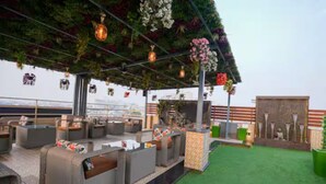 Un salon sur le toit avec des espaces de détente en plein air, une zone recouverte d’un gazon synthétique et des guirlandes lumineuses décoratives.