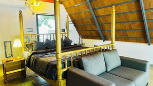 A four-poster bed with a wooden frame, a grey sofa, a bedside table with a lamp, and a window with a view of greenery. - Oh-Bali Villa by Travent Mug (Ramanagara)