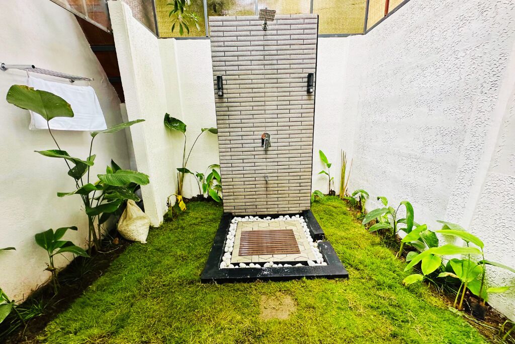Un petit jardin clos, avec un mur recouvert de carreaux, un élément décoratif aquatique et une série de pierres plates servant de marchepied.