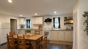 A modern kitchen with white cabinets, a wooden dining table, and a stove. - Charming 2BR Guest House w/ Pool - Perfect Getaway (West Tisbury)