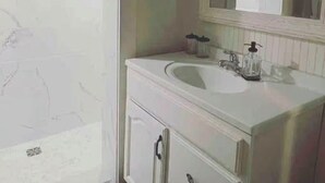 A bathroom with a shower, a sink, a mirror, and a cabinet. - Charming 2BR Guest House w/ Pool - Perfect Getaway (West Tisbury)
