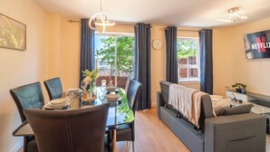Ein modernes Wohnzimmer mit Essbereich, einer Couch, einem Flachbildfernseher und Blick ins Freie.