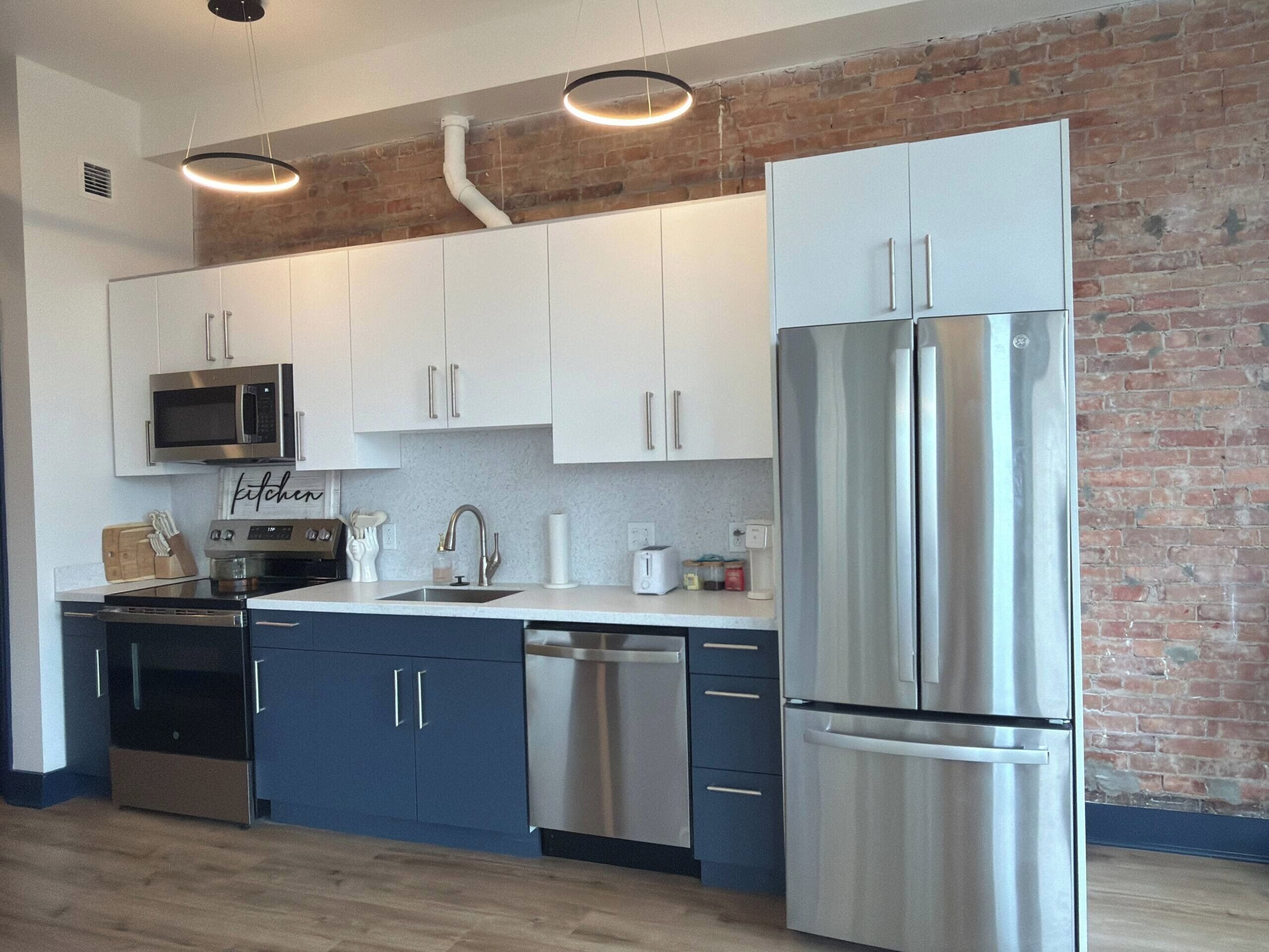 A modern kitchen with white cabinets, stainless steel appliances, and a brick wall.
