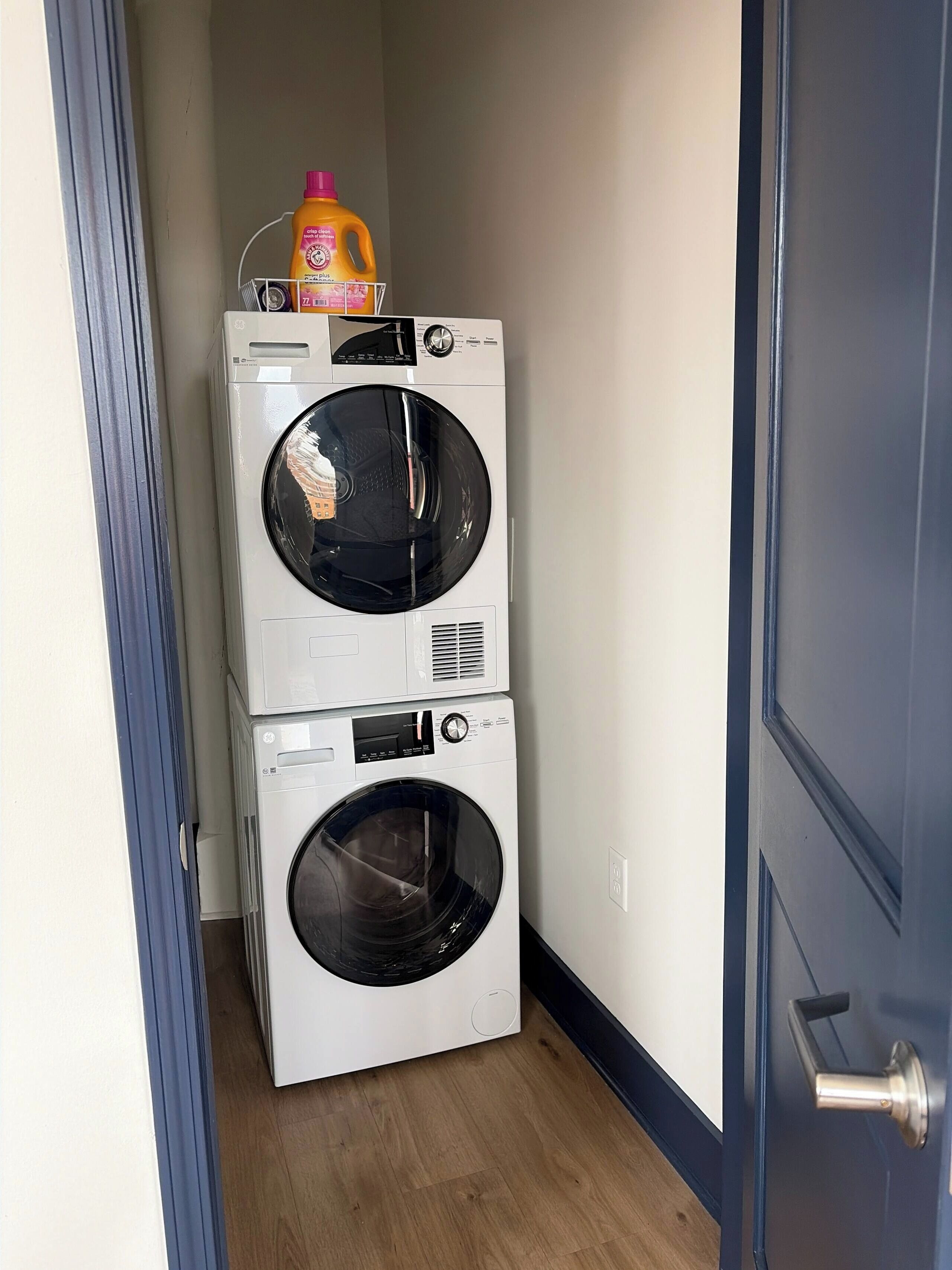 A laundry room with two stacked washing machines and a detergent bottle.