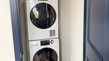 A laundry room with two stacked washing machines and a detergent bottle.