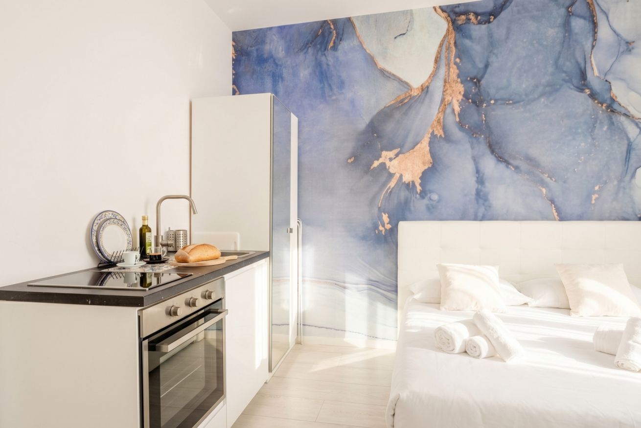 Une chambre d’hôtel moderne avec un coin cuisine, un lit avec une literie blanche et un mur en marbre.