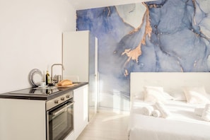 Quarto de hotel moderno com cozinha, cama com roupa de cama branca e parede de mármore.
