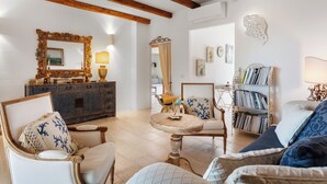Ein Wohnzimmer mit Sofa, Sesseln, Couchtisch, Bücherregal und Spiegel.