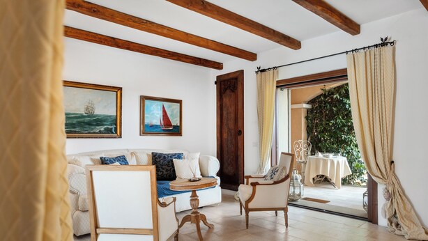 Ein Zimmer mit Holzboden, einer Couch, einem Sessel, einem kleinen Tisch und einer Tür zu einem Außenbereich mit Tisch und Stühlen.