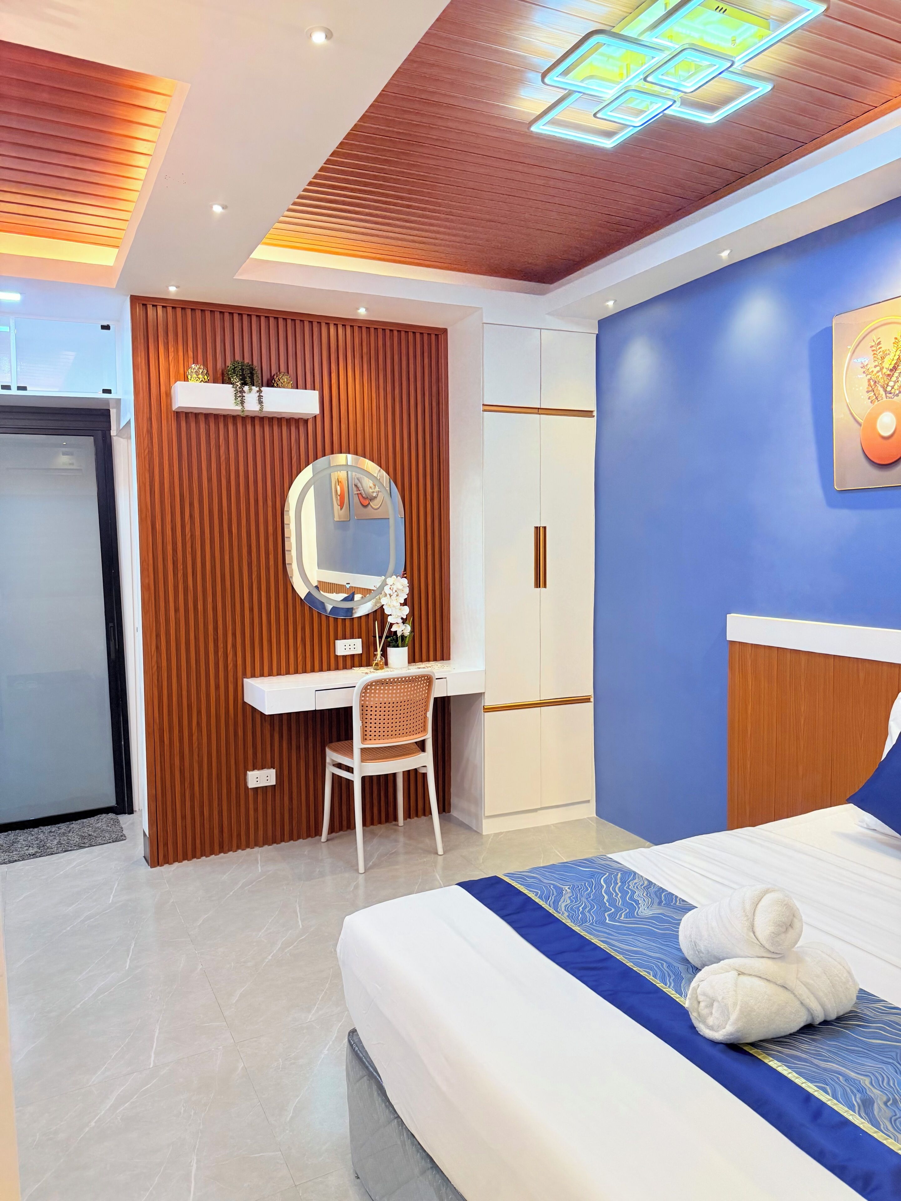 A modern hotel room with a bed, a desk, a chair, a wardrobe, and a mirror.