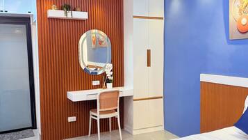A modern hotel room with a bed, a desk, a chair, a wardrobe, and a mirror.