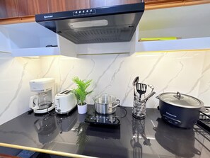 Ett kök med en kaffebryggare, brödrost, en krukväxt, en kastrull och köksredskap på en svart bänkskiva.