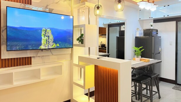 A modern kitchen with a flat-screen TV mounted on the wall, wooden paneling, and a dining area with black stools. - New Condotel-Inspired Studio with
Hot & Cold Shower, 10 minutes SM Mall (General Santos City (Dadiangas))