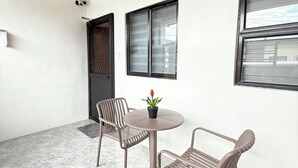 A room with a wooden ceiling, a tiled floor, two chairs, a small table with a potted plant, and a window with blinds. - New Condotel-Inspired Studio with
Hot & Cold Shower, 10 minutes SM Mall (General Santos City (Dadiangas))