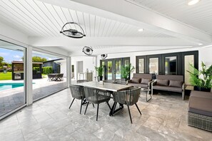 A spacious patio area with a dining table and chairs, a sofa, and a pool in the background. - McCarty Mansion - Fort Pierce Waterfront Paradise - 7Br/6Ba - Sleeps 20 (Fort Pierce)