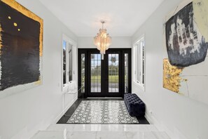 Un pasillo con candelabro, puertas con marco negro y alfombra estampada.