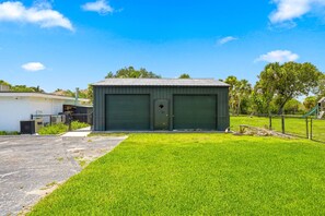 A small, single-story building with a green shuttered garage door, surrounded by a well-maintained lawn and a chain-link fence. - McCarty Mansion - Fort Pierce Waterfront Paradise - 7Br/6Ba - Sleeps 20 (Fort Pierce)