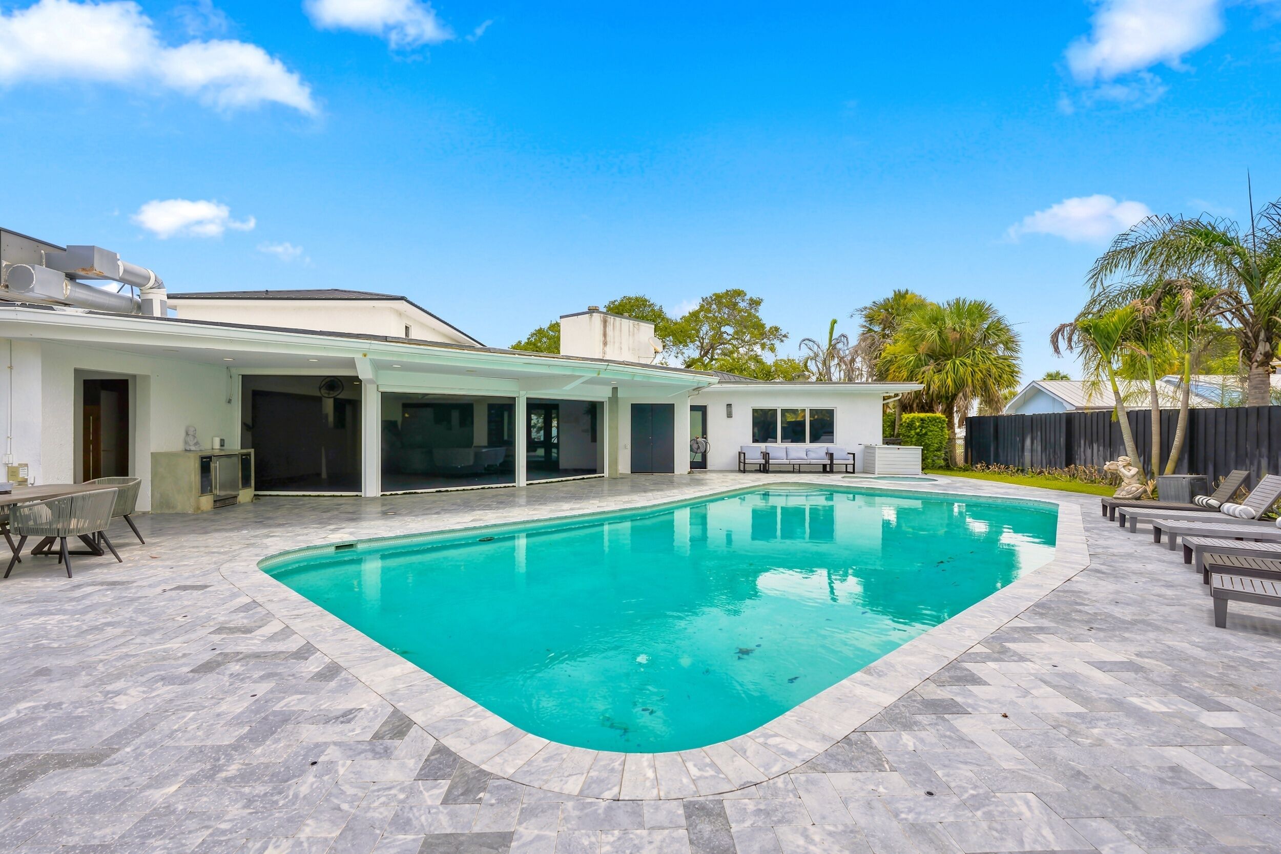 A modern outdoor swimming pool with a herringbone tile pattern, surrounded by a covered patio area with seating.