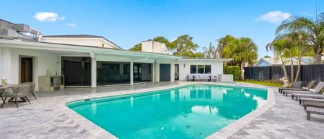 A modern outdoor swimming pool with a herringbone tile pattern, surrounded by a covered patio area with seating.