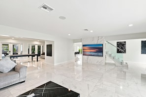 A spacious living area with a marble floor, a pool table, and a large painting of a sunset over the ocean. - McCarty Mansion - Fort Pierce Waterfront Paradise - 7Br/6Ba - Sleeps 20 (Fort Pierce)