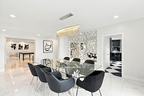 A modern dining area with a glass table, black chairs, and a decorative wall with mirrors. - McCarty Mansion - Fort Pierce Waterfront Paradise - 7Br/6Ba - Sleeps 20 (Fort Pierce)
