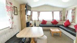 A caravan interior with a sofa, a table, a TV, and a lamp. - J J Caravan (Abergele)