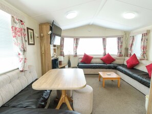 A caravan interior with a sofa, a table, a TV, and a lamp. - J J Caravan (Abergele)