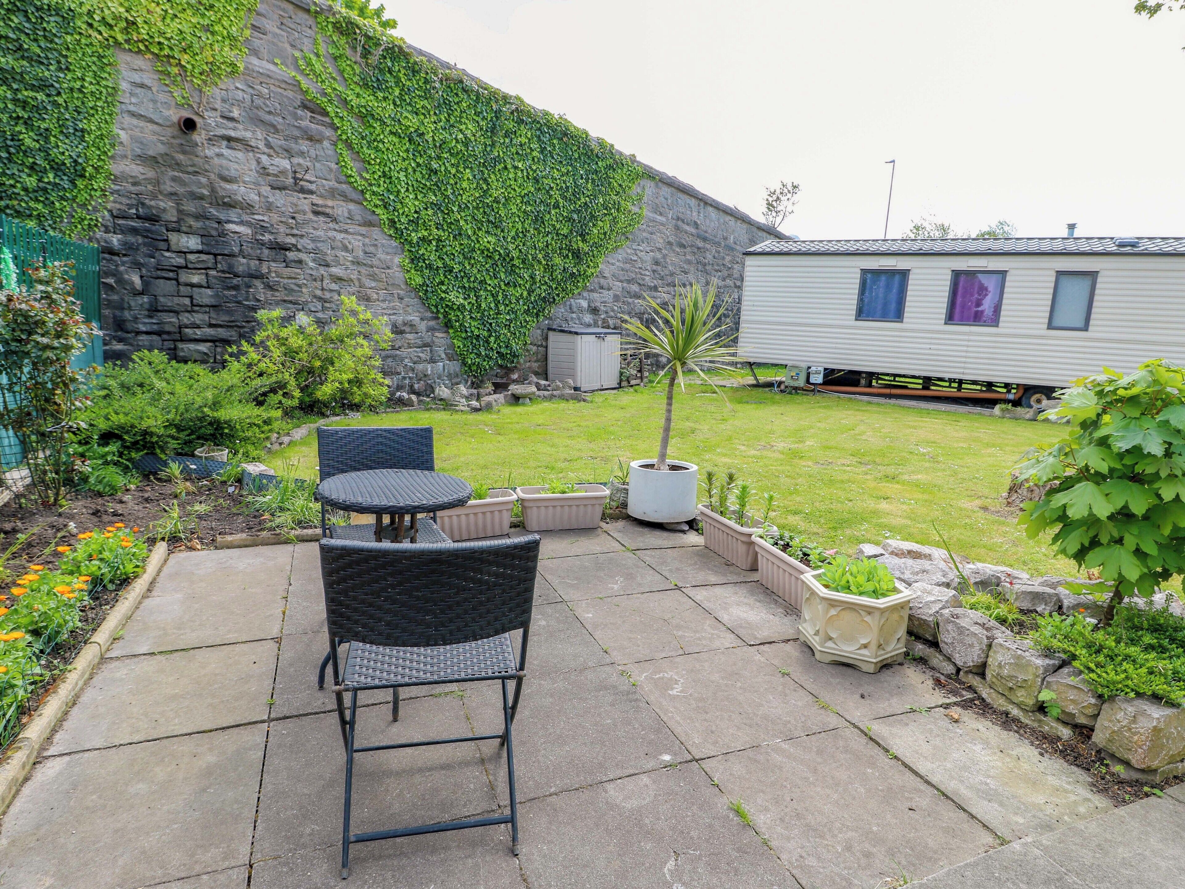 A patio with outdoor furniture, a stone wall, and a mobile home in the background.