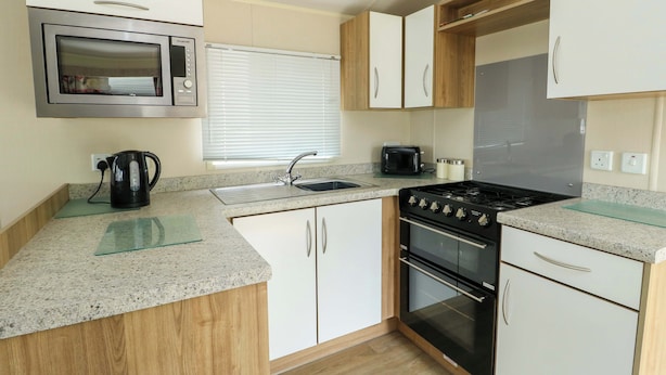 A compact kitchen with a microwave, stove, sink, and cabinets. - J J Caravan (Abergele)
