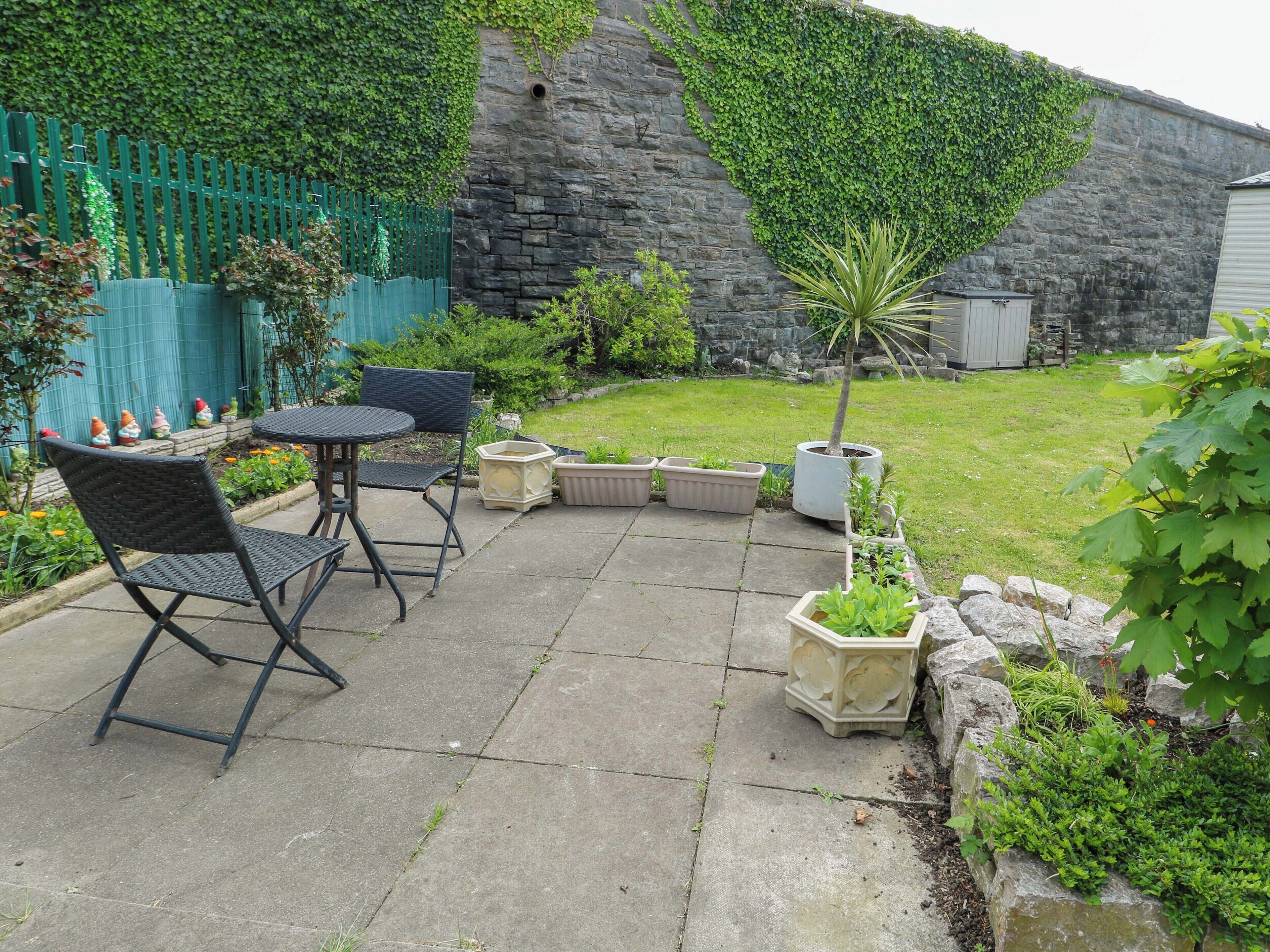 A patio with a table and chairs, potted plants, and a stone wall.