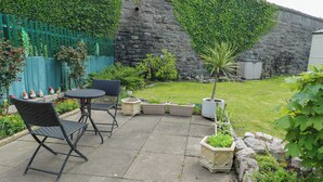 A patio with a table and chairs, potted plants, and a stone wall. - J J Caravan (Abergele)