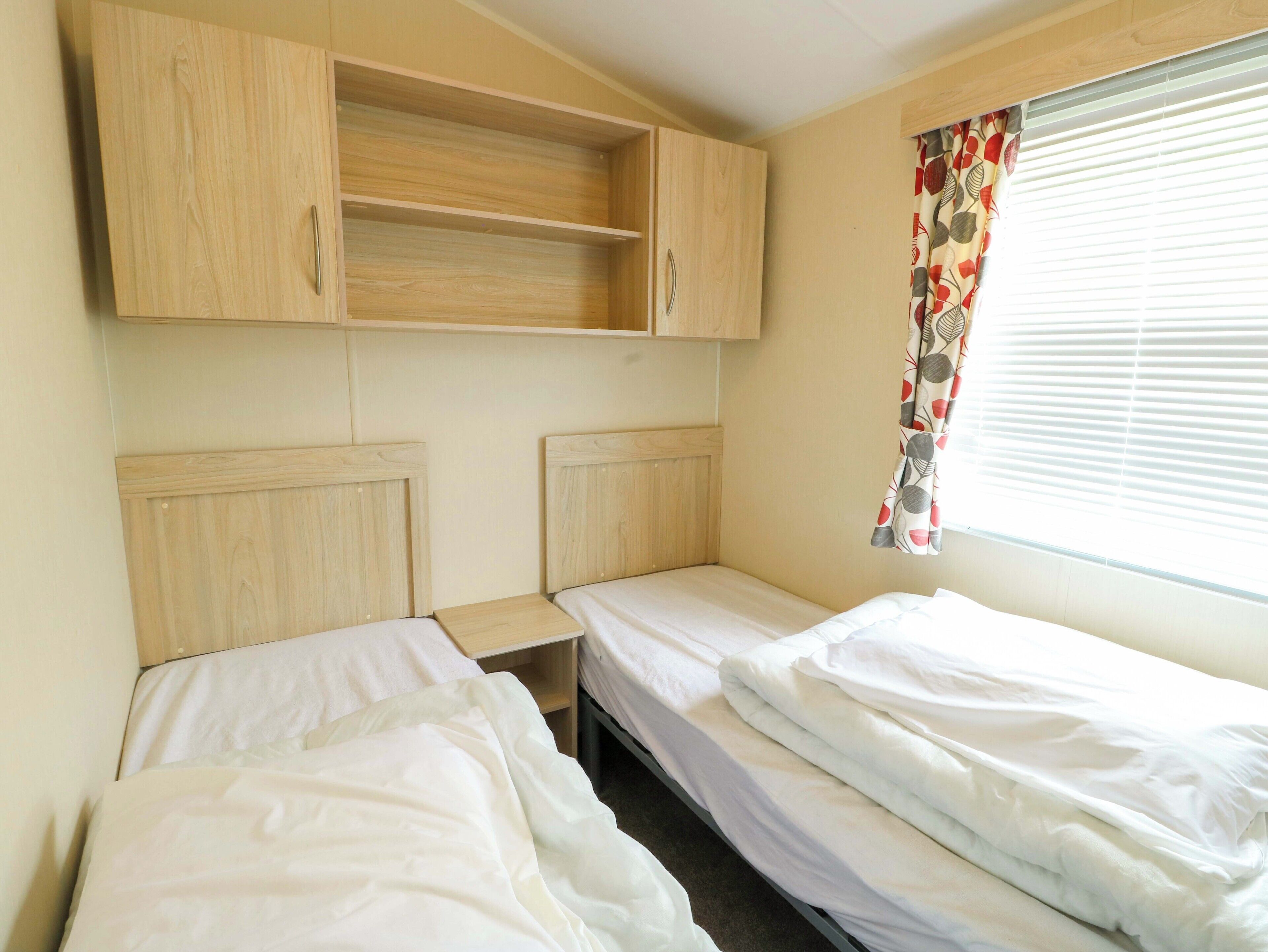 Habitación con dos camas, cabeceros de madera, una mesita y una ventana con cortina.