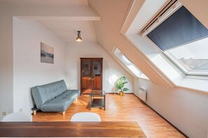 A loft-style room with a high ceiling, a grey sofa, a small table, a potted plant, and a skylight. - 2 Bedroom Apartment in Antwerp (Antwerp)