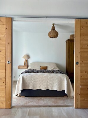 A bedroom with a bed, a hanging light fixture, a bedside table with a lamp, and a wooden wardrobe. - Seaside cocoon renovated top floor 180-degree view. Air conditioning and private parking. (Ajaccio)