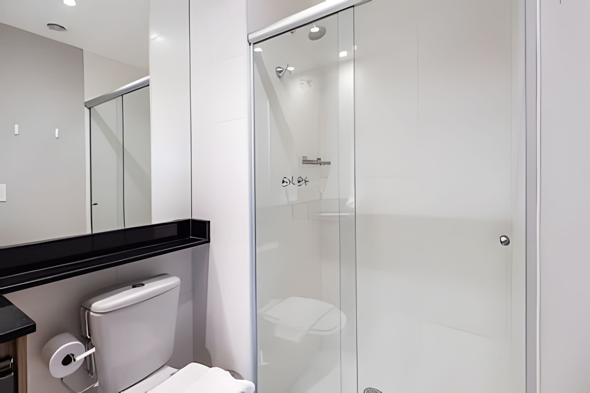 Ein modernes Badezimmer mit Duschkabine aus Glas, Toilette und Waschbecken mit schwarzer Ablagefläche.
