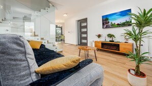 Uma sala de estar moderna com sofá, mesa de centro, televisão, escada e planta em vaso.