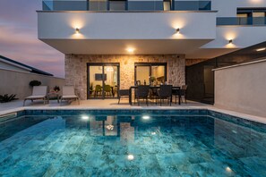 A modern pool area with a stone wall, outdoor seating, and a clear pool. - Seaview Villa Mar with pool, jacuzzi and sauna (Privlaka)
