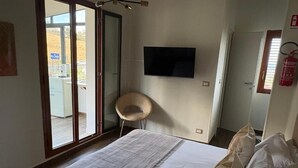 A bedroom with a bed, a chair, a TV, and a sliding door to a balcony. - Civico 2o la casa di nina (Reggio Calabria)