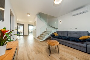 A modern living room with a staircase, a grey sofa, and a wooden coffee table. - Seaview Villa Sal with pool, jacuzzi and sauna (Privlaka)