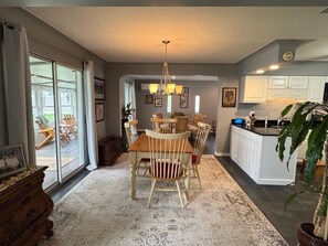 A dining area with a wooden table and chairs, a chandelier, and a kitchen with white cabinets.